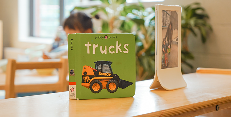 A board book called Trucks by Priddy Books with a skid-steer loader truck on the green cover is on top of a bookshelf in a YMCA Child Care centre.