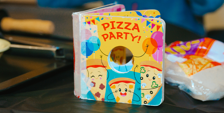 A small yellow and blue picture book called Pizza Party is on a table in a YMCA Child Care centre classroom.