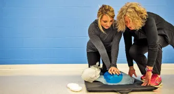 A trainer helping a student perform CPR on a dummy