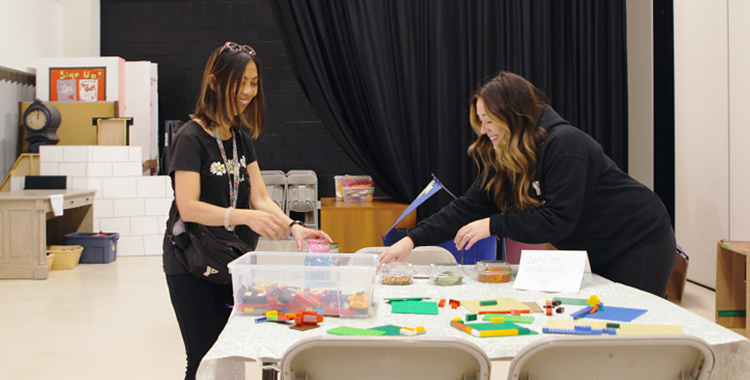 Two educators prepare toys on a table for Before & After School child care.