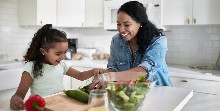 Smiling child and parent preparing food in kitchen. Child is assisting parent in cutting zucchini. They are at home.