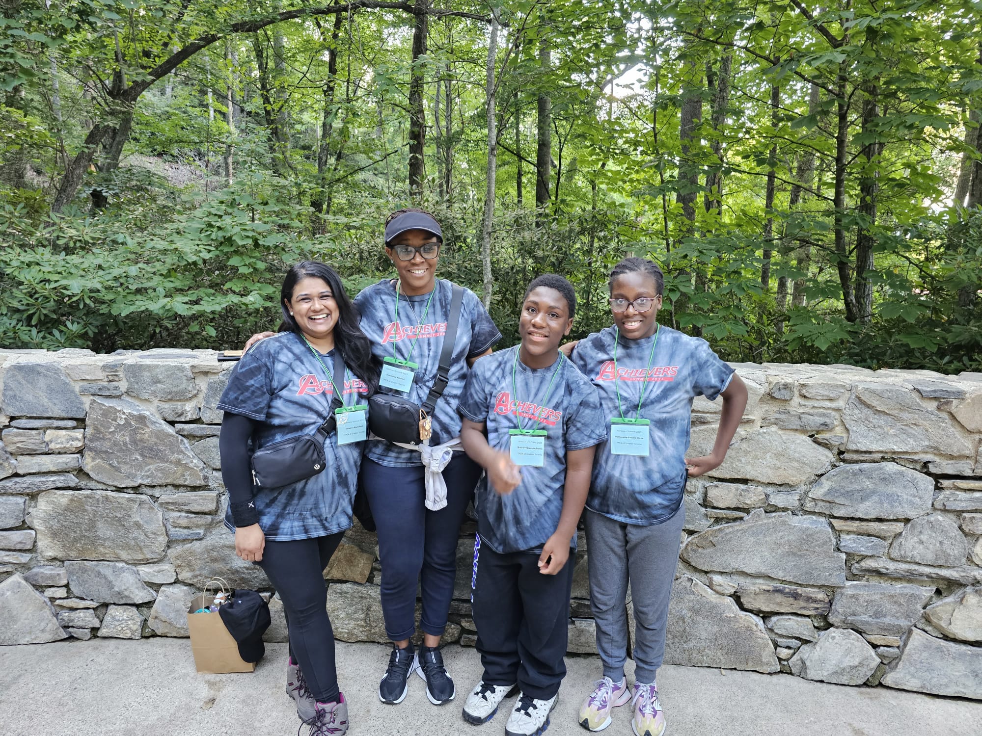 Two program participants are standing with two staff members. Trees line the background
