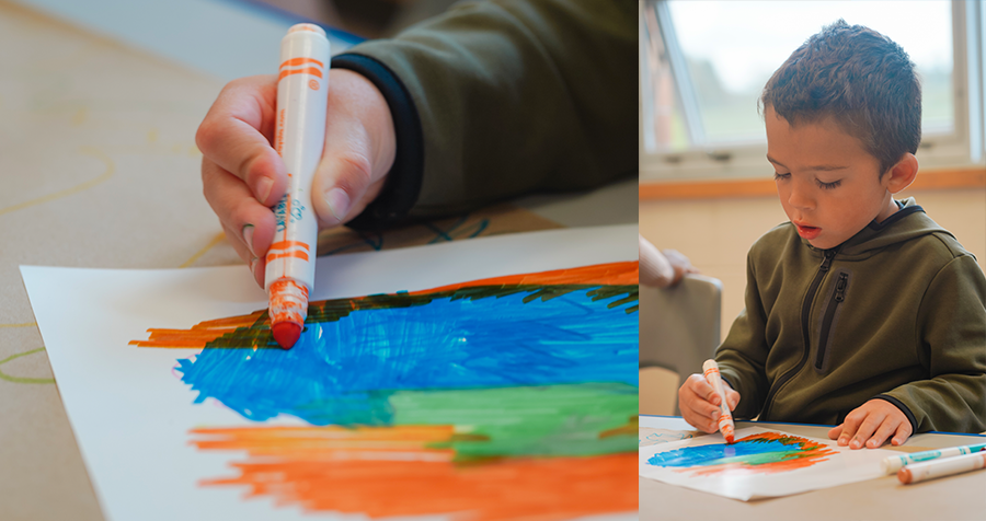 A child colours on paper with an orange marker.