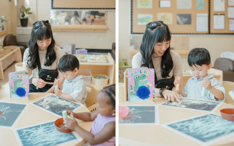 A colourful Dino Chores children's board book featuring a green dinosaur stands on a table beside a seated adult and several printed images.