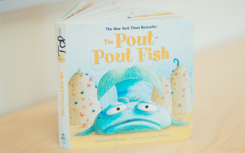 Text: The Pout-Pout Fish. Graphic: A blue fish with a pouty expression on the cover of a children's board book standing on a wooden table.