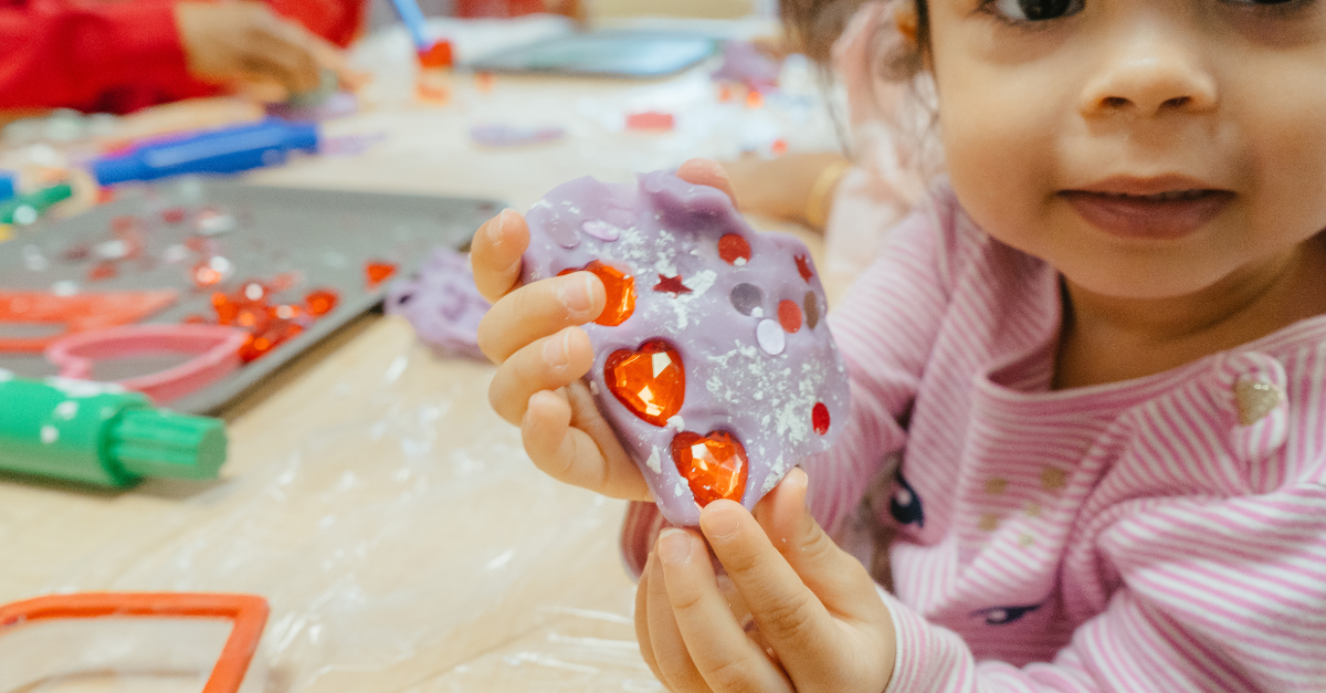 A child holds lavender cloud dough decorated with red heart gems and stickers.