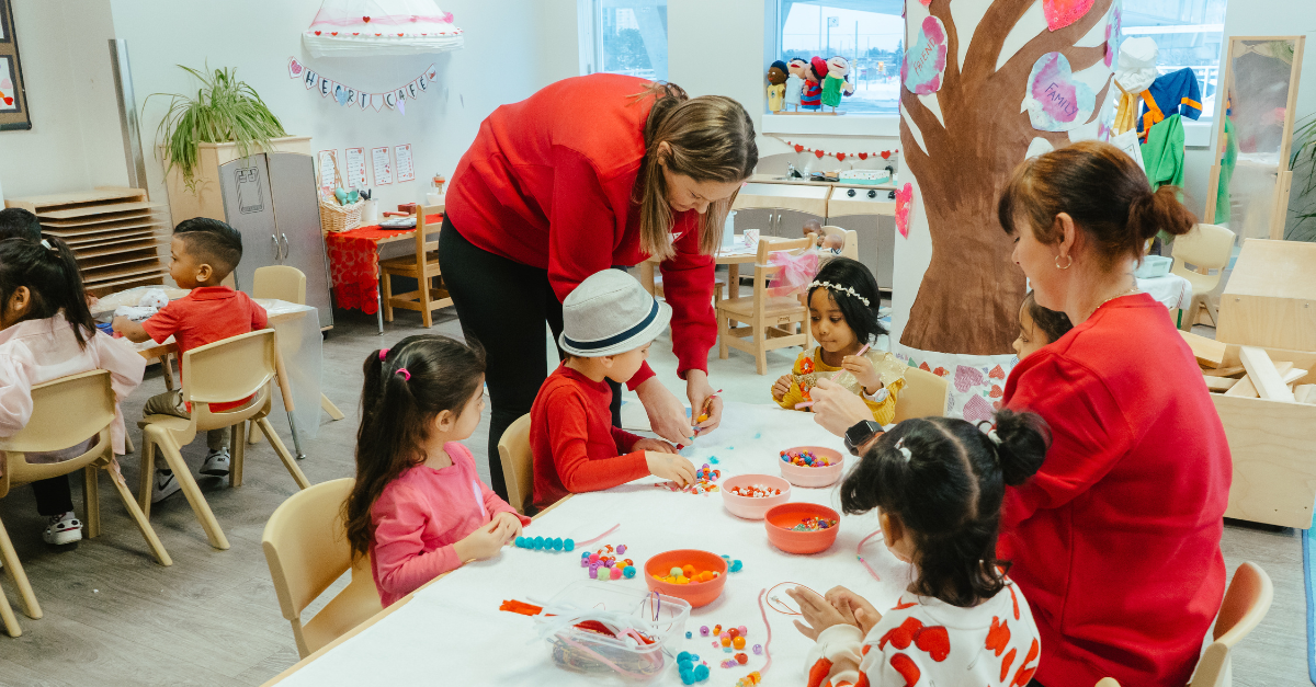 A group of children and two educators work together on a friendship bracelet project in a colourful Valentine’s Day classroom.