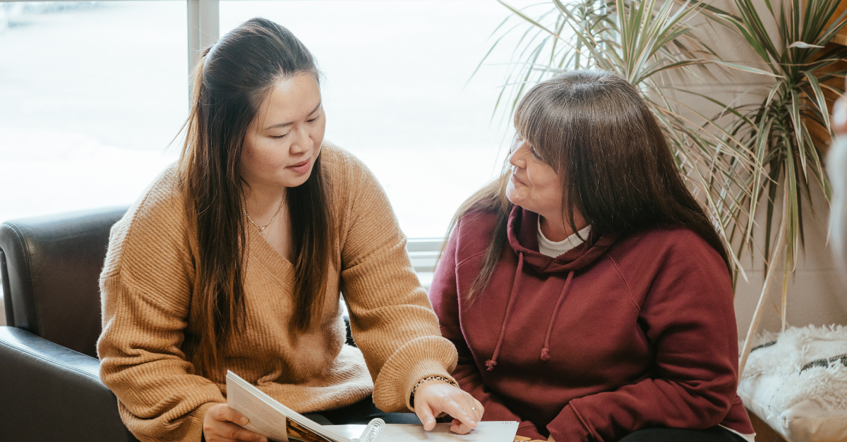 Jennifer, wearing a brown knit sweater, shows another educator a page in a curriculum booklet.