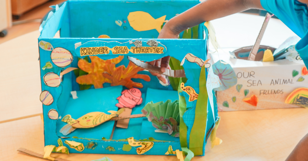 Child creating a colourful ocean-themed diorama called “Kinder Sea Theatre” during a YMCA child care art activity.