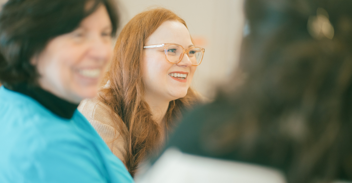 Alyssa, wearing glasses, smiles while in conversation with two other educators.