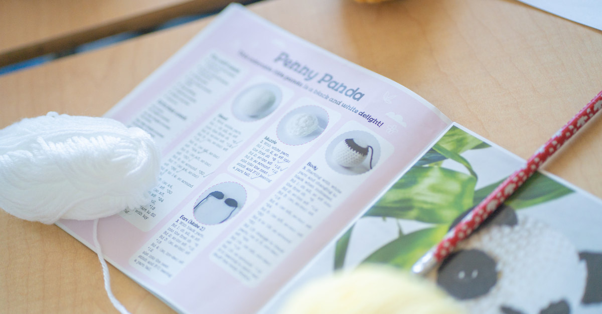 An open book shows instructions for a panda crochet project beside a ball of white yarn.