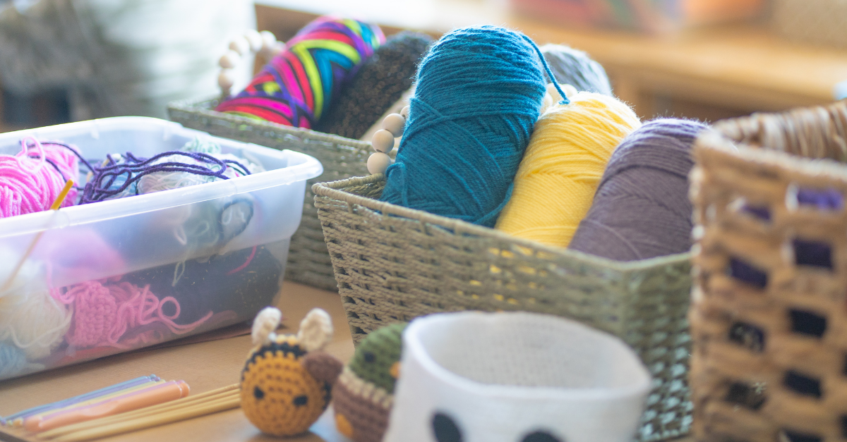 Colourful yarn and completed crochet projects, including a bee, a duck, and a small bucket, are arranged with plastic needles and materials.