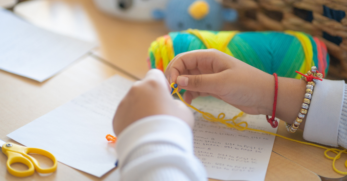 A child begins a crochet project using multicoloured thread, with handwritten notes from an educator placed below.