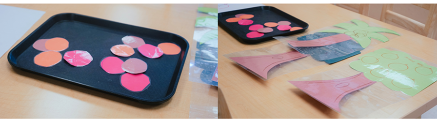 Paper cut outs of a palm tree, and apple tree with individual cut-outs of apples, coconuts, and oranges on a black tray in a YMCA child care classroom.