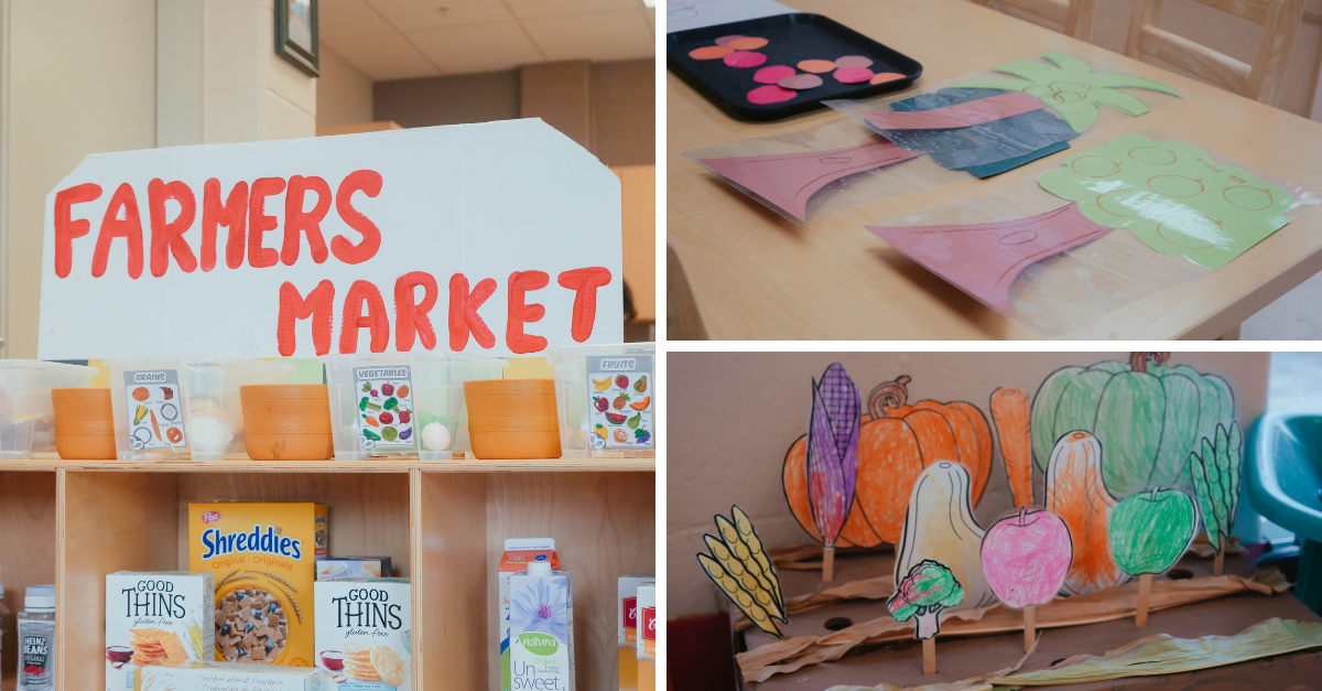 Classroom farmers' market play setup featuring a handmade "Farmers Market" sign above shelves with bins labelled grains, vegetables, and fruits. Nearby are children’s paper cutouts of fruits and vegetables, a tray of play coins, and laminated produce shapes used for imaginative play.