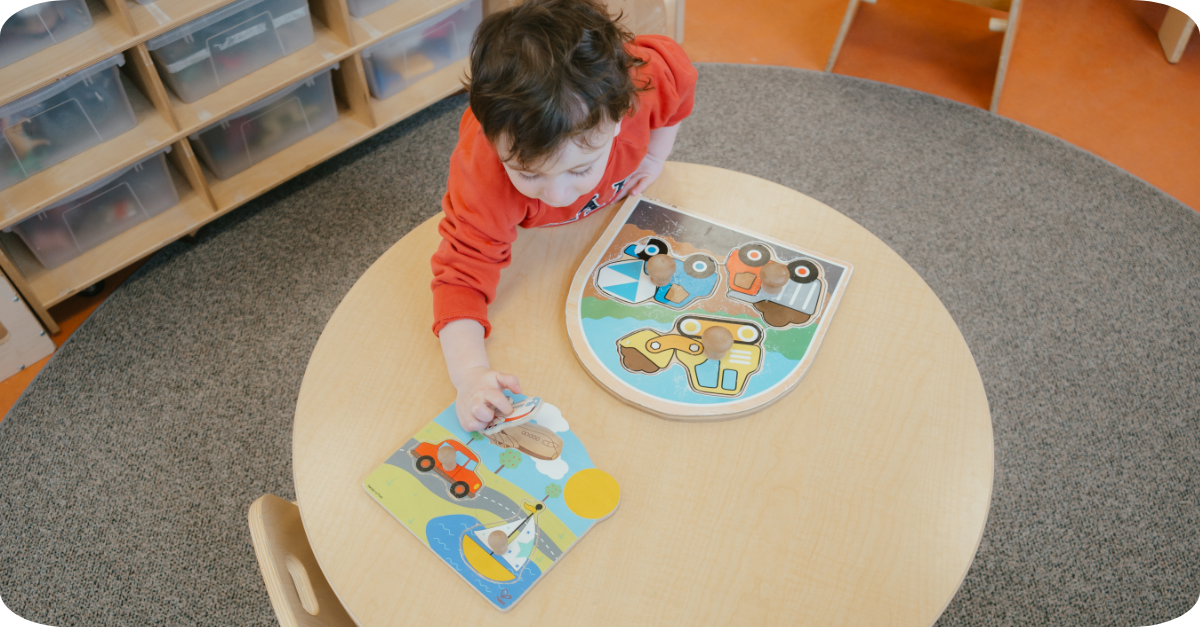 Child completing a construction and beach car puzzle at a toddler-height table in a YMCA child care room.