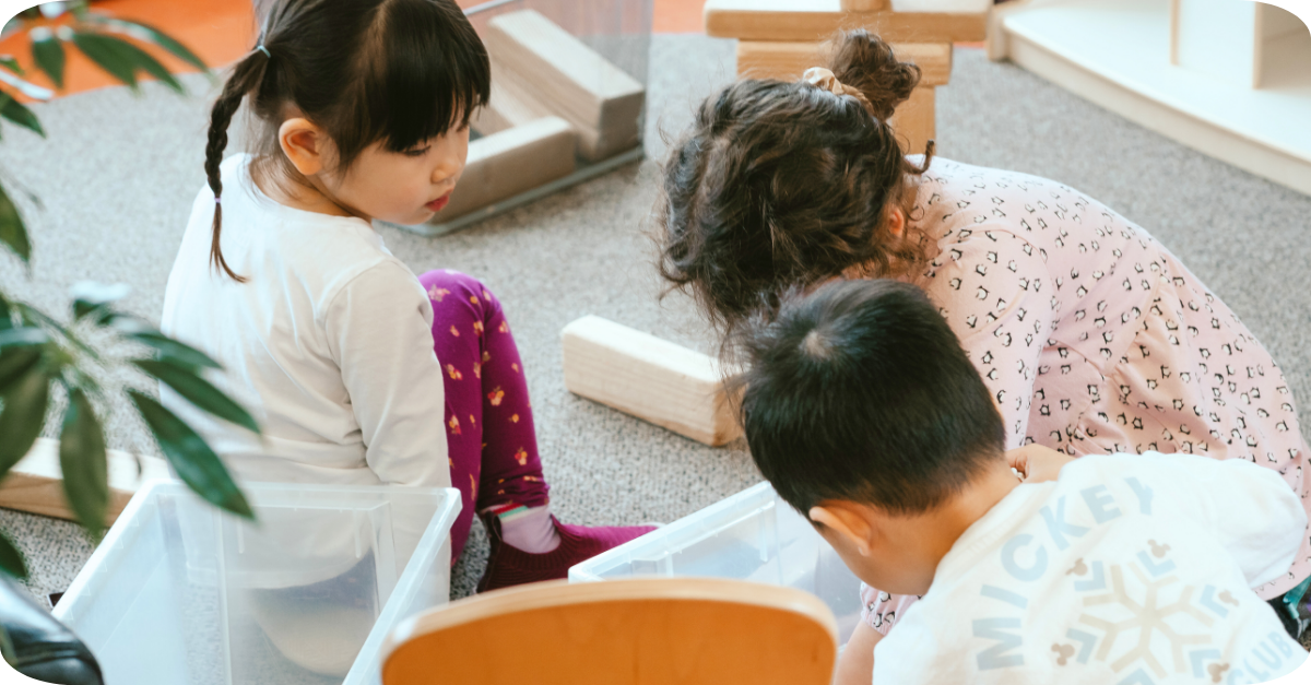Three children building together with wooden blocks on a carpet in a YMCA room.