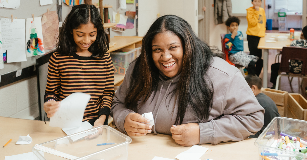Shianne and a child smile together while doing a craft activity in a before and after school classroom.