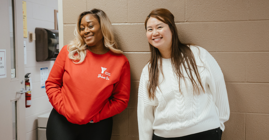 Susan and Jenny stand side by side, smiling in a YMCA hallway.