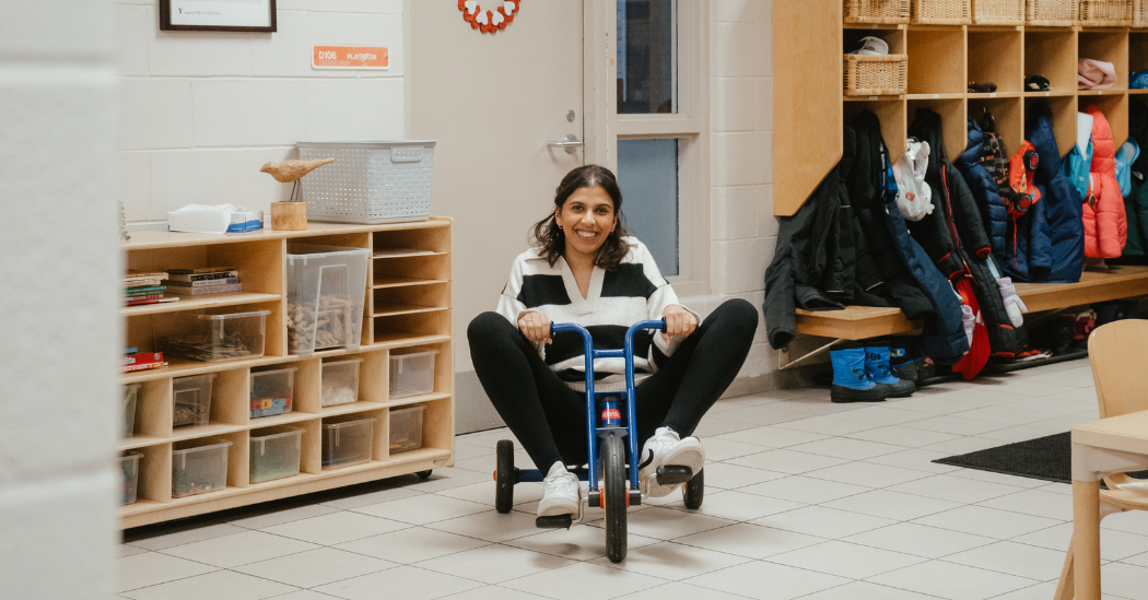 Petra, a YMCA supervisor, rides a tricycle down a child care hallway.