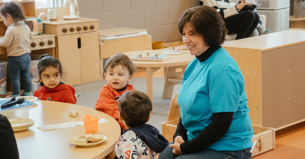 Valerie interacts with three toddlers inside a child care room.