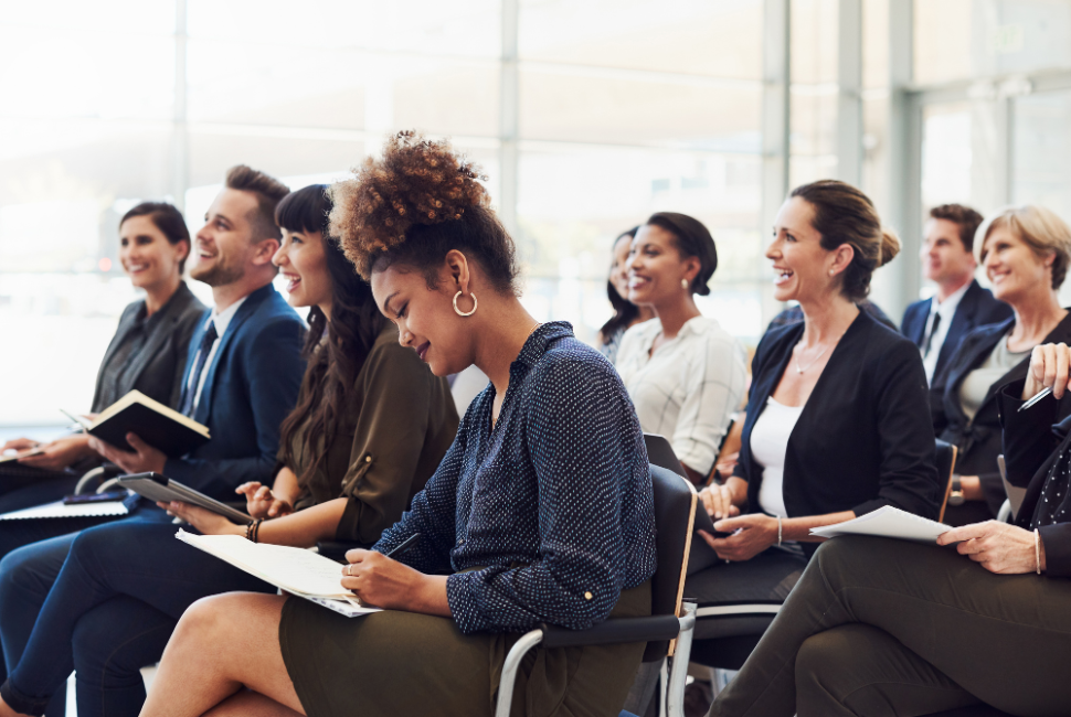 A group of people are seated and taking notes, listening to a speaker