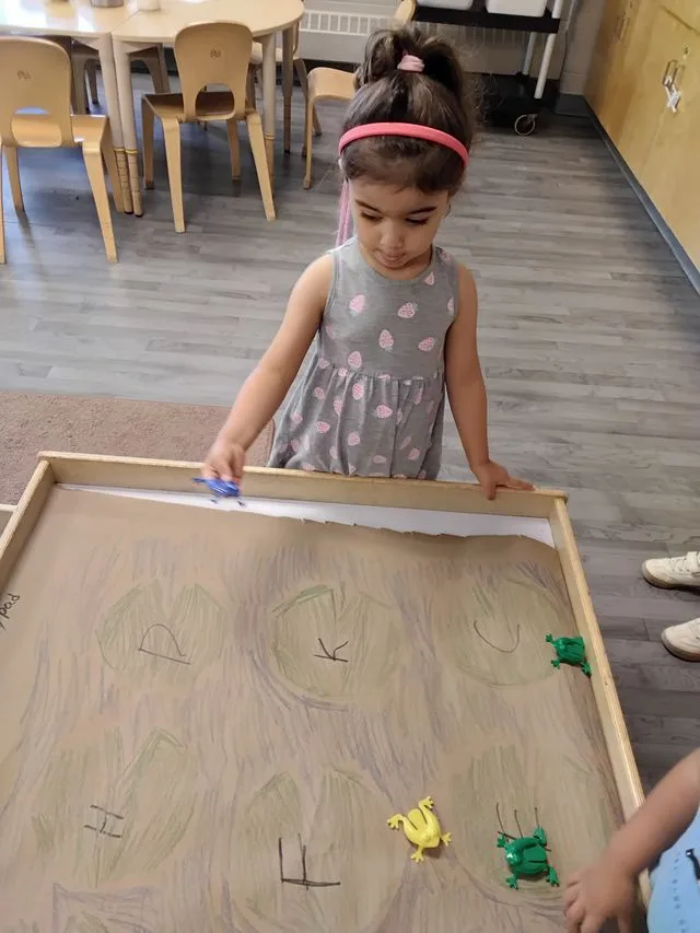 A child in a pink hairband and grey dress plays at a table in a child care centre