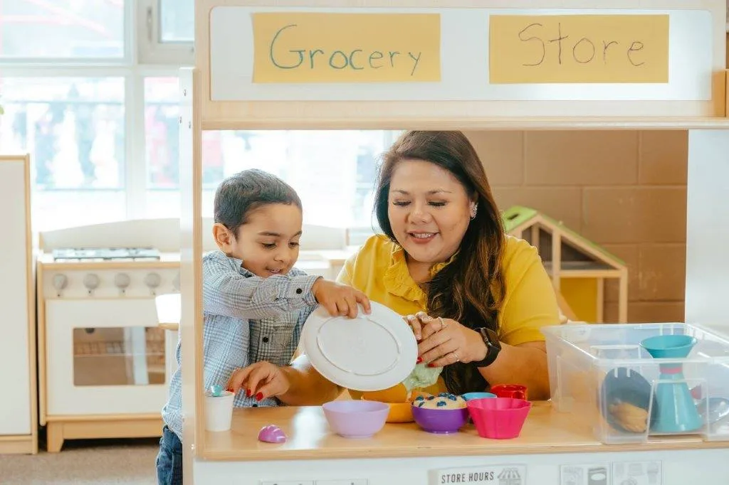 A child care educator and young child play in a pretend grocery store setting.