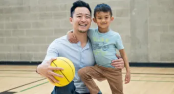 happy parent and child posing with a basketball on an indoor basketball court
