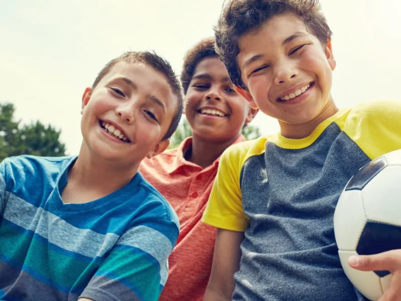 Three campers outdoor, smiling. One camper is holding a soccer ball