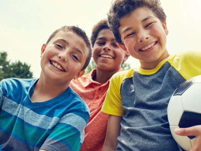 Three campers outdoor, smiling. One camper is holding a soccer ball 