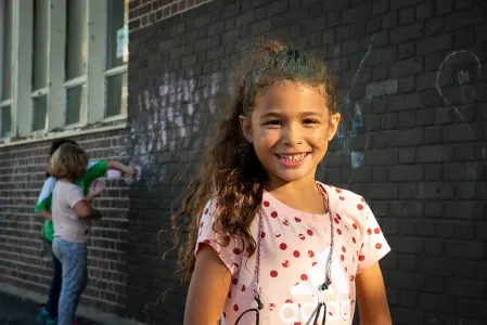a girl smiling, while children in the background draw with chalk on the wall