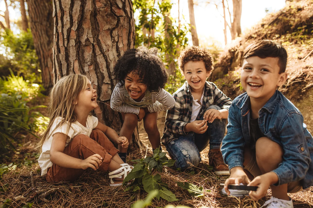 Group of cute kids sitting together in forest and looking at camera. Cute children playing in woods