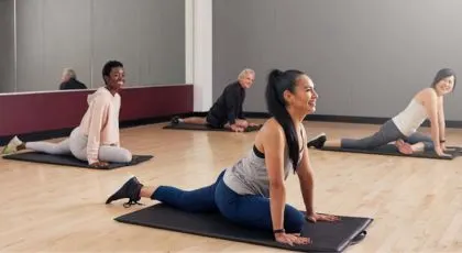 A group fitness yoga class in session, with four people in pigeon pose on mats.