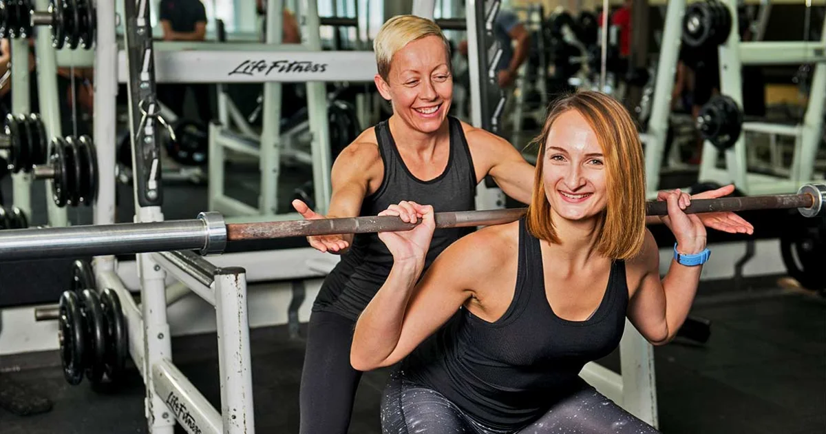 A woman helping another woman train with weights