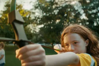 camper holding a bow and arrow outside at camp.