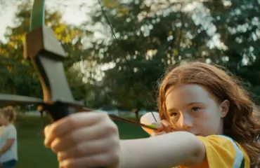 camper holding a bow and arrow outside at camp.