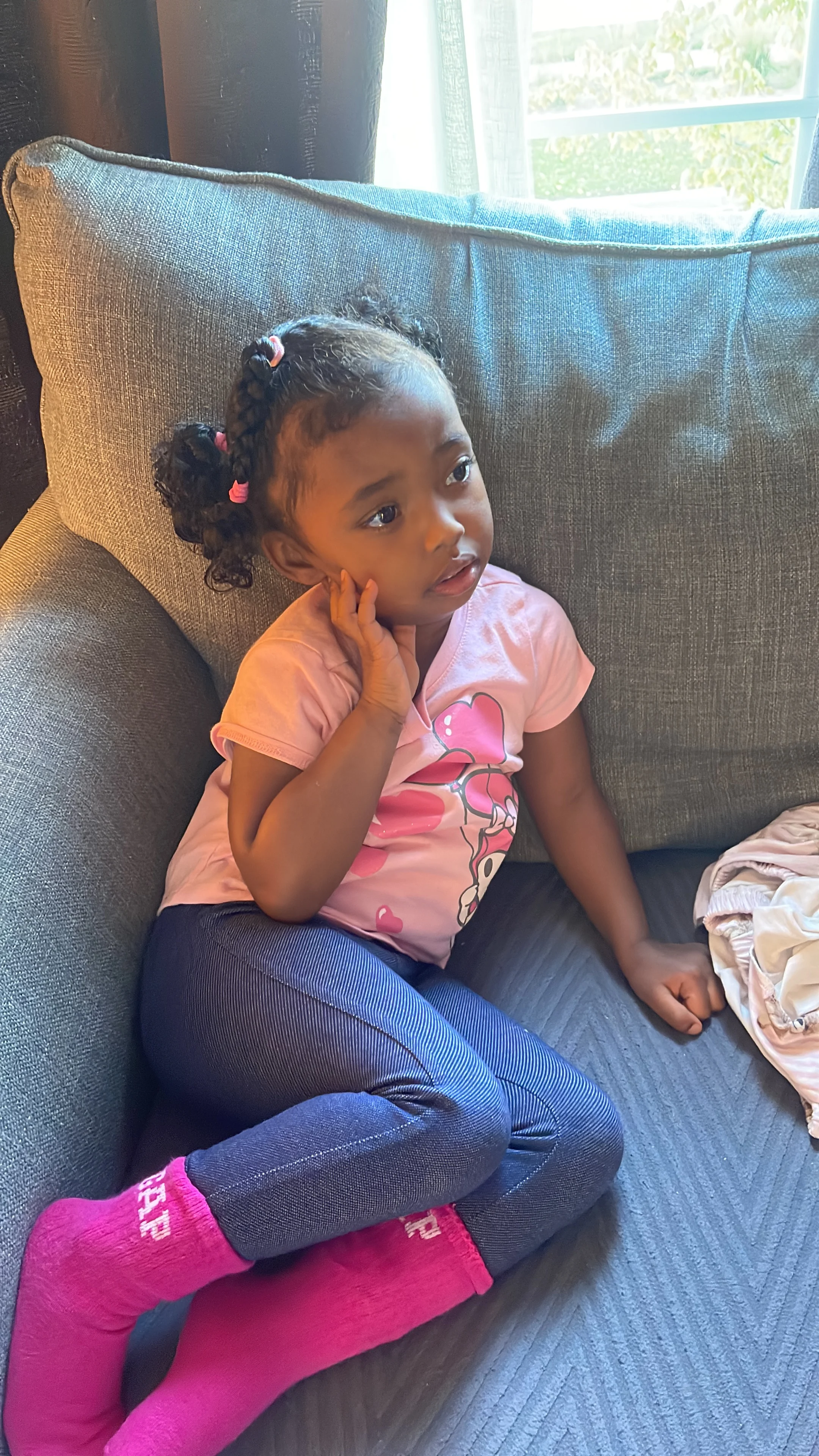 A child with braided hair and pink tshirt sits on a blue couch.