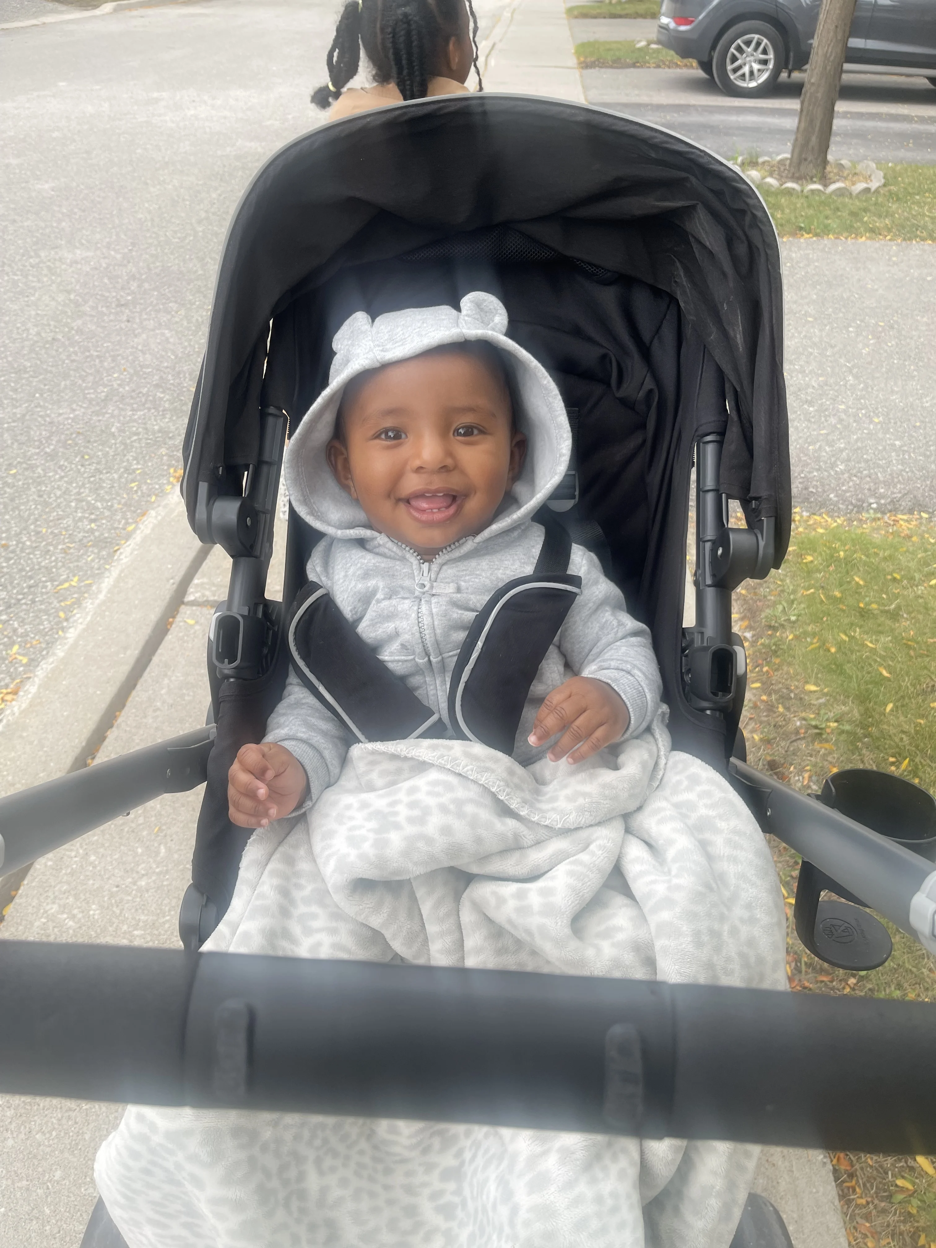 A smiling infant in a grey hooded top sits in their stroller.