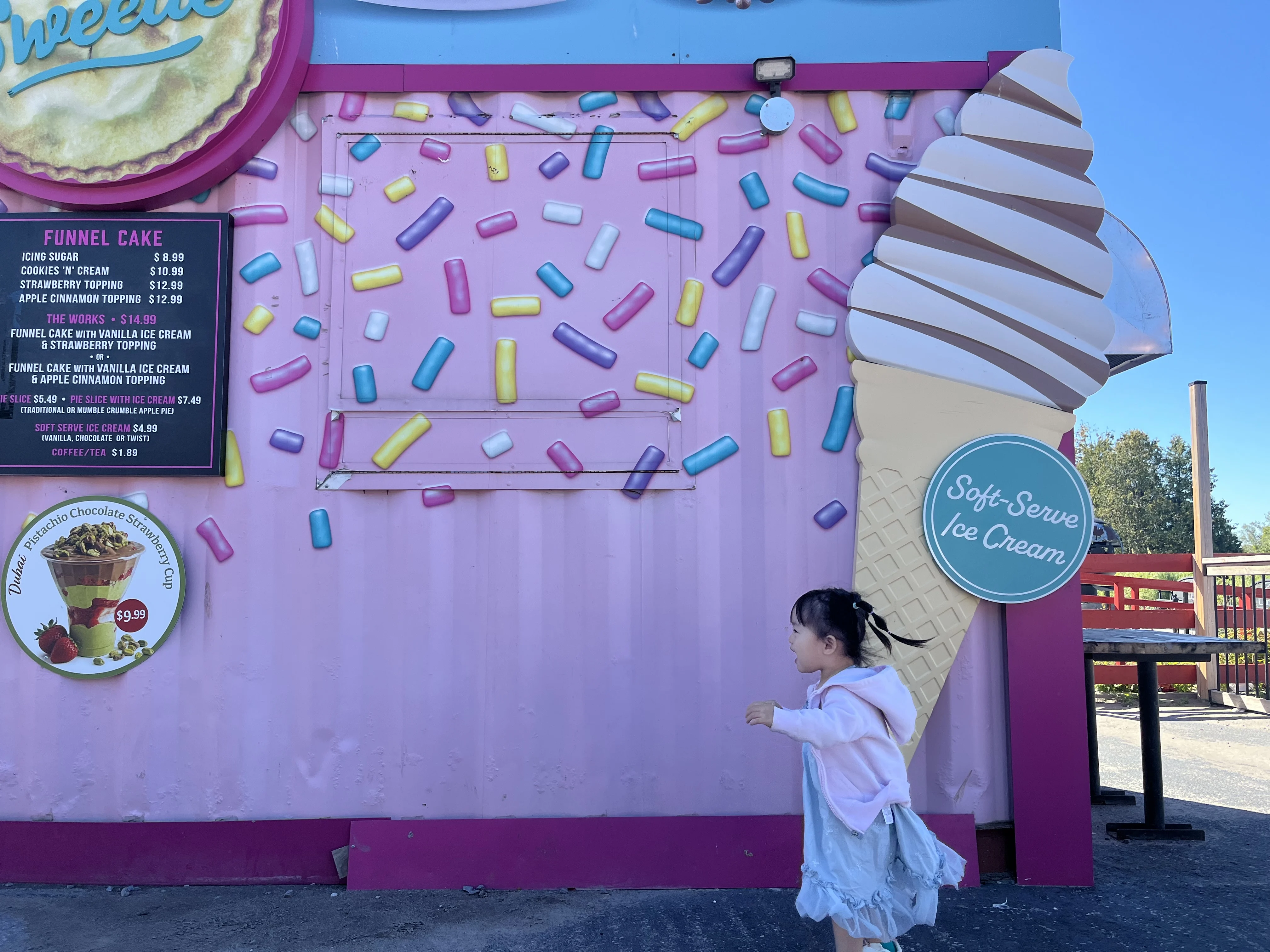 A young child with pigtails runs by a large sign advertising ice cream