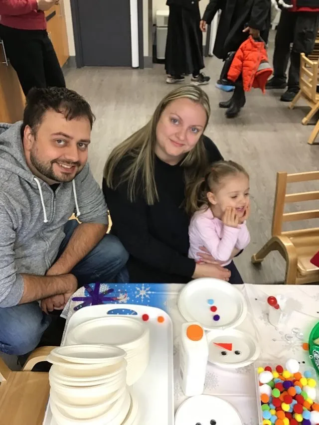 Two adults sit with a young child in front of table of crafts. All are smiling.