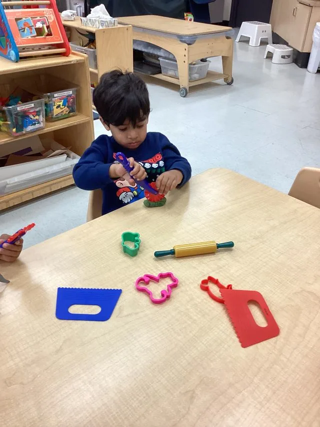 A young child sits at a table in a child care centre playing with toy tools.