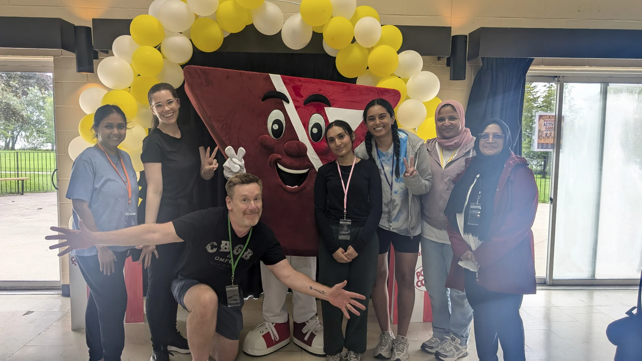 Six child care educators stand in front of the YMCA mascot, a large letter-Y with a eyes, an nose and smiling mouth