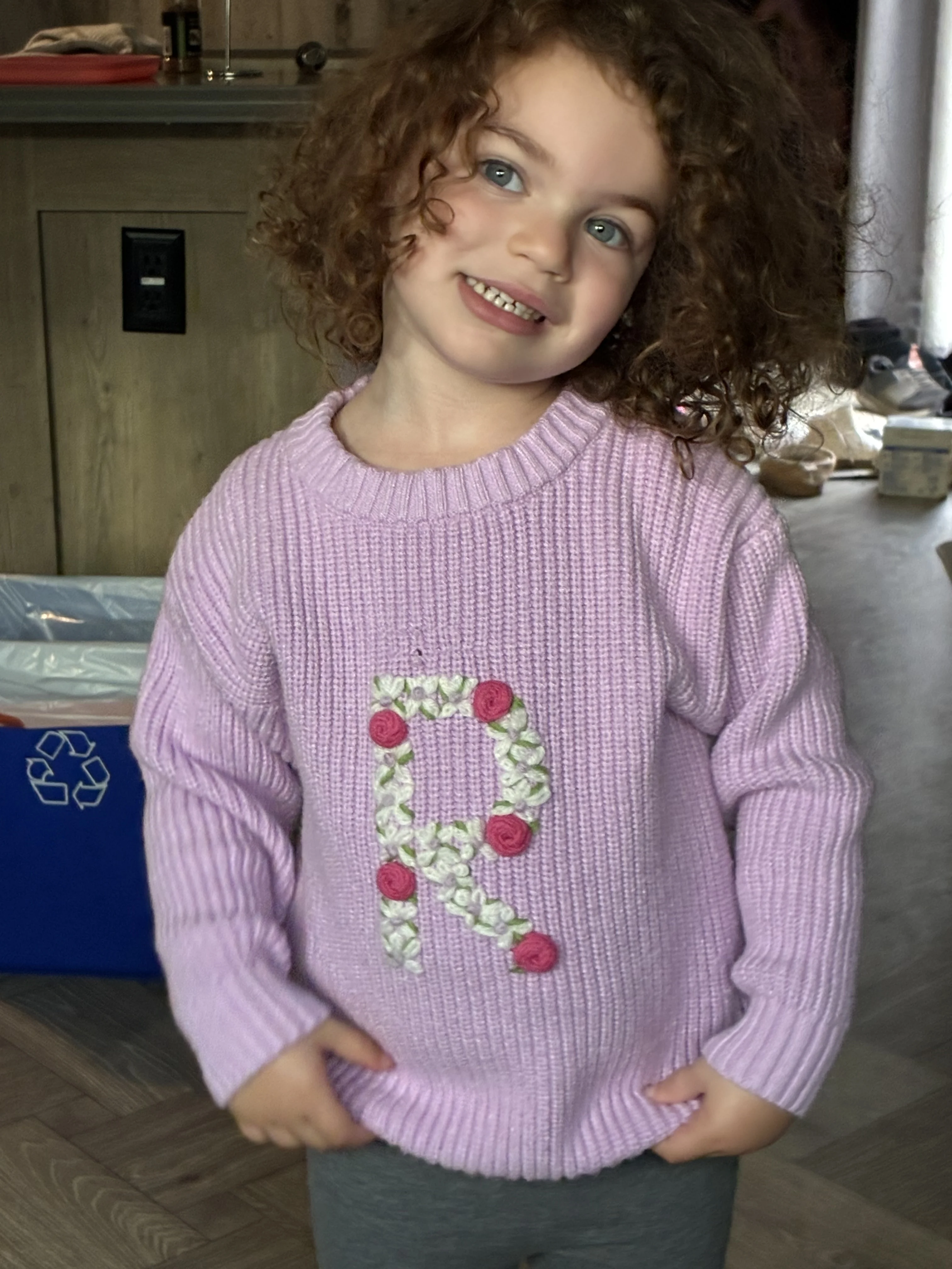 A young smiling child with curly shoulder-length hair and purple sweater