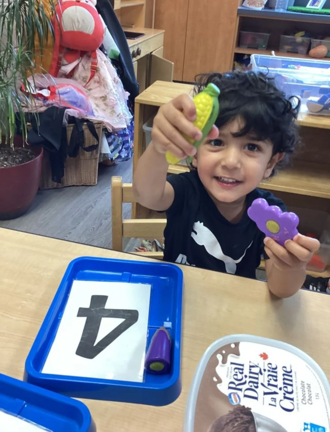 A young child with dark hair smiles as they play with small plastic toys in child care room 