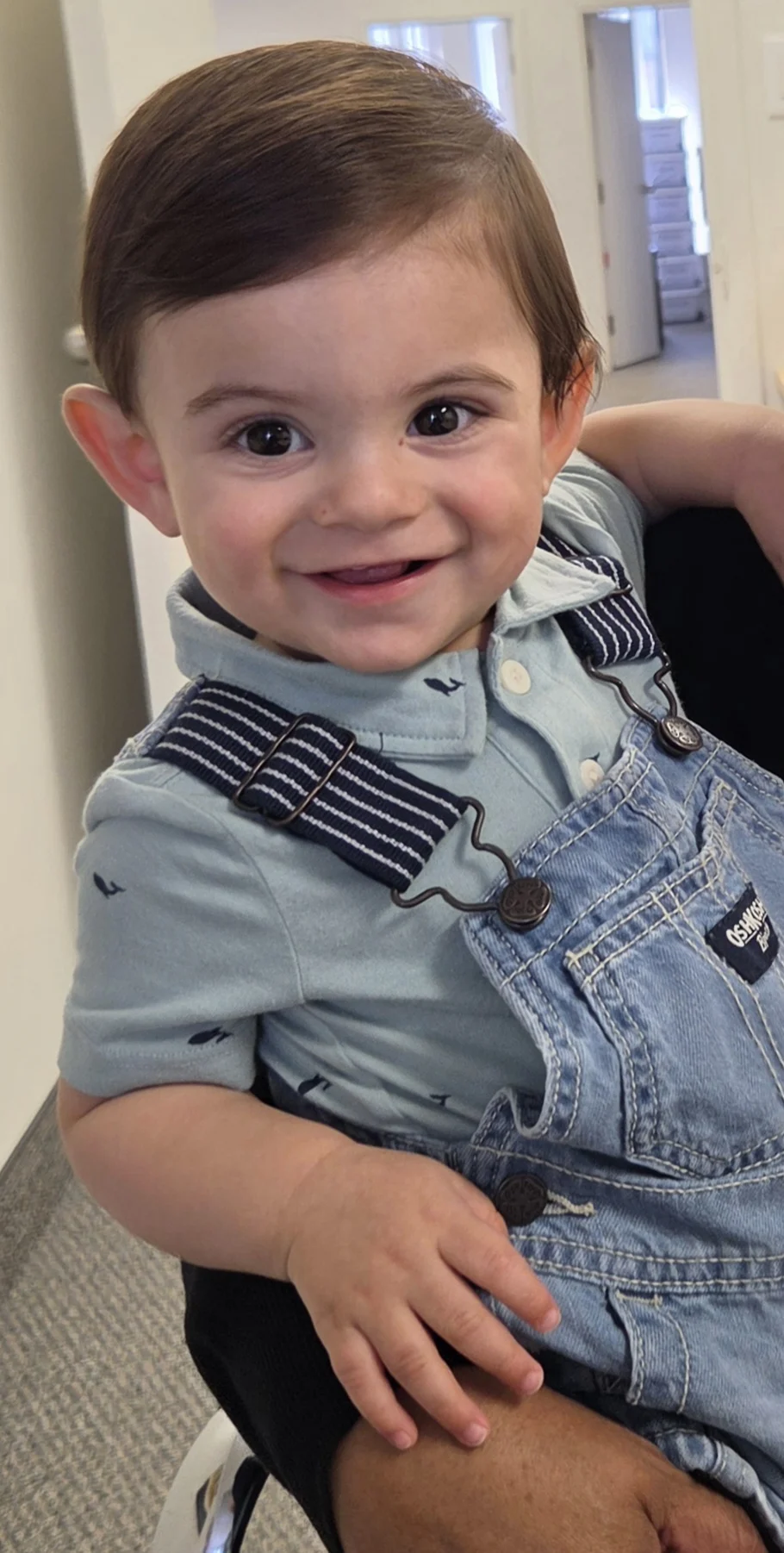 A young child in a blue top and overalls smiles.
