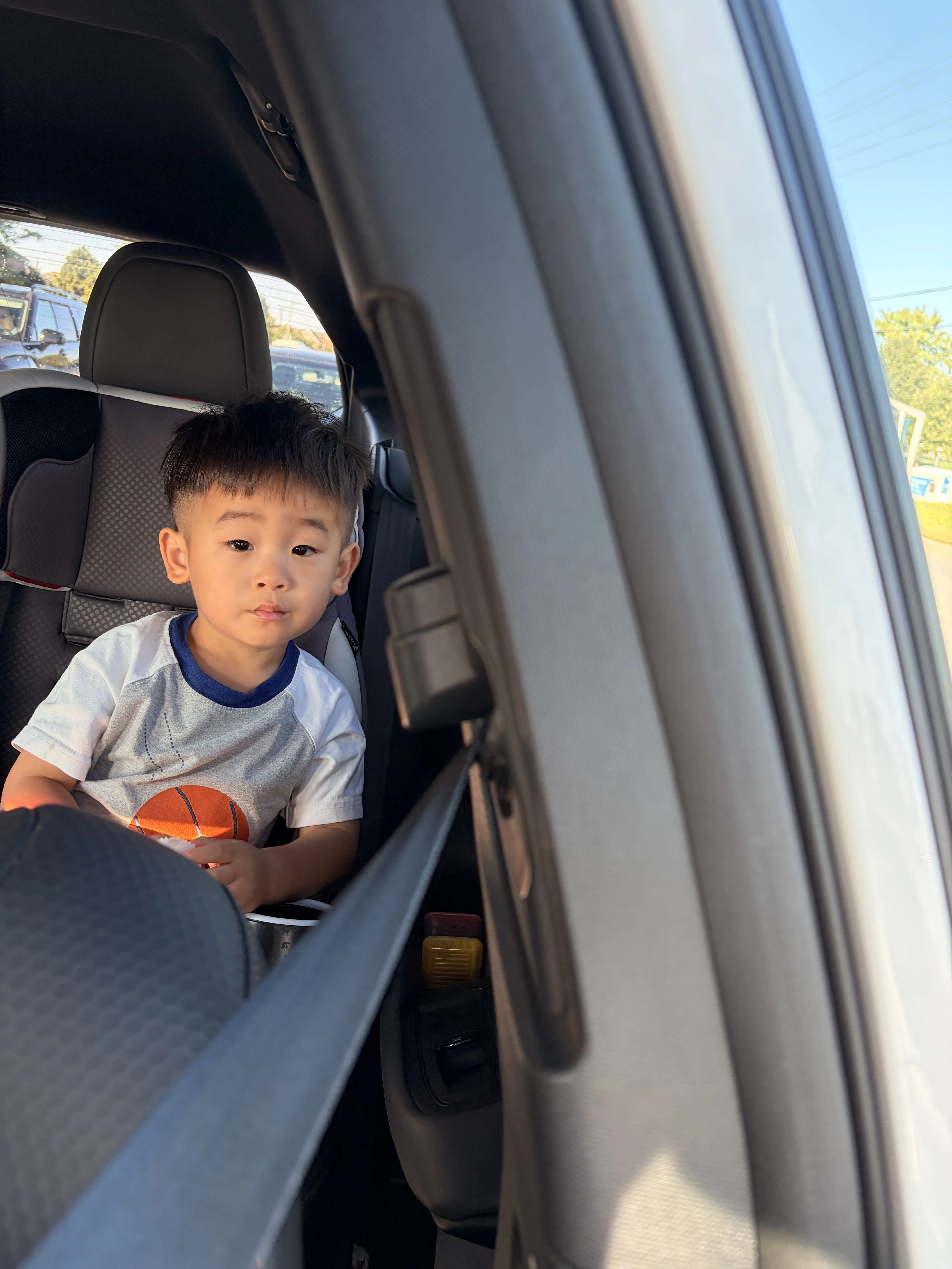 A young child in a white t-shirt sits in the backseat of a car.