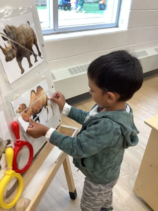 A young child in a hooded sweat shirt is doing a puzzle game with pictures of zoo animals.