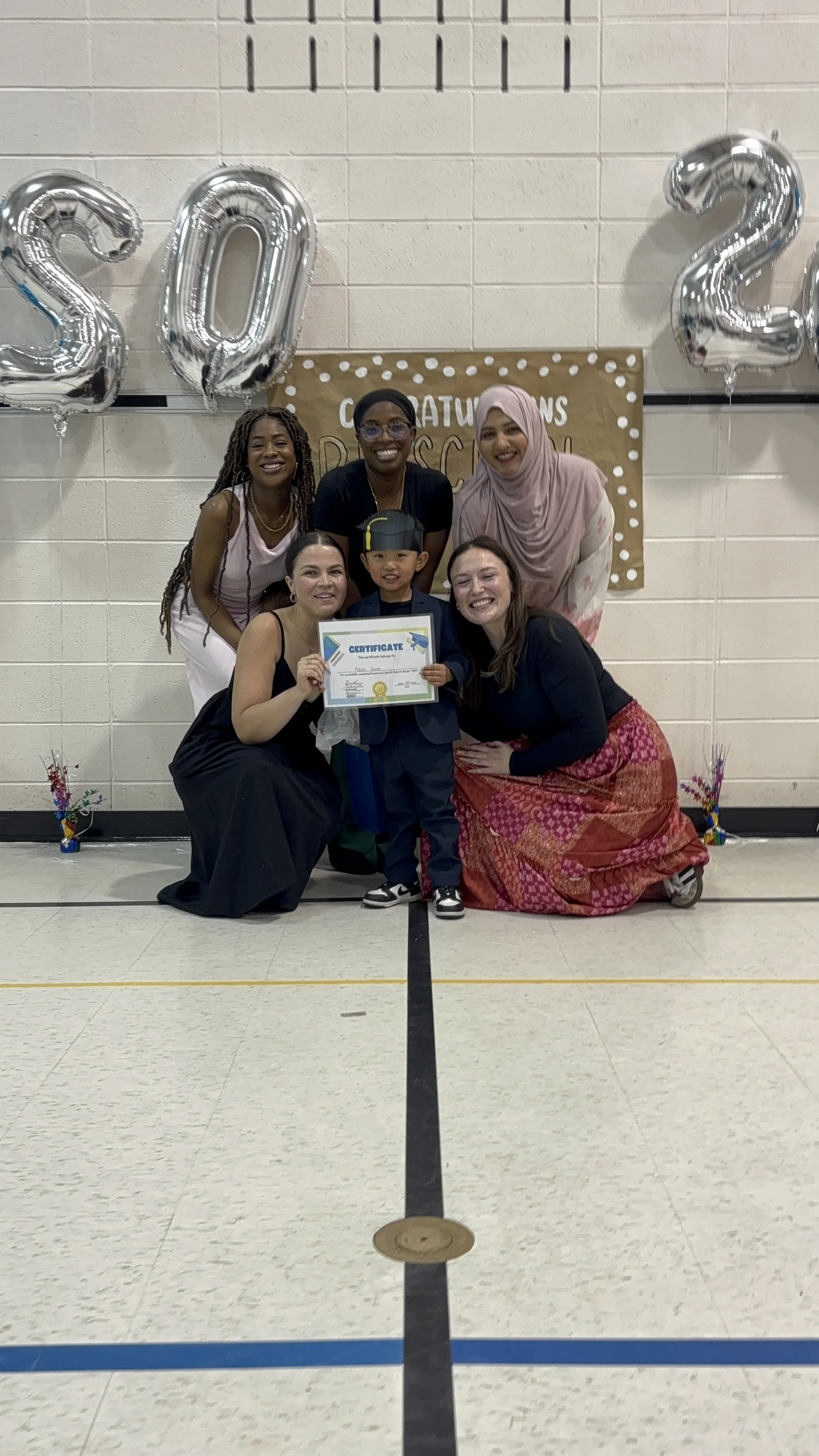 Five adults pose for a picture with a graduating preschooler holding a certificate.