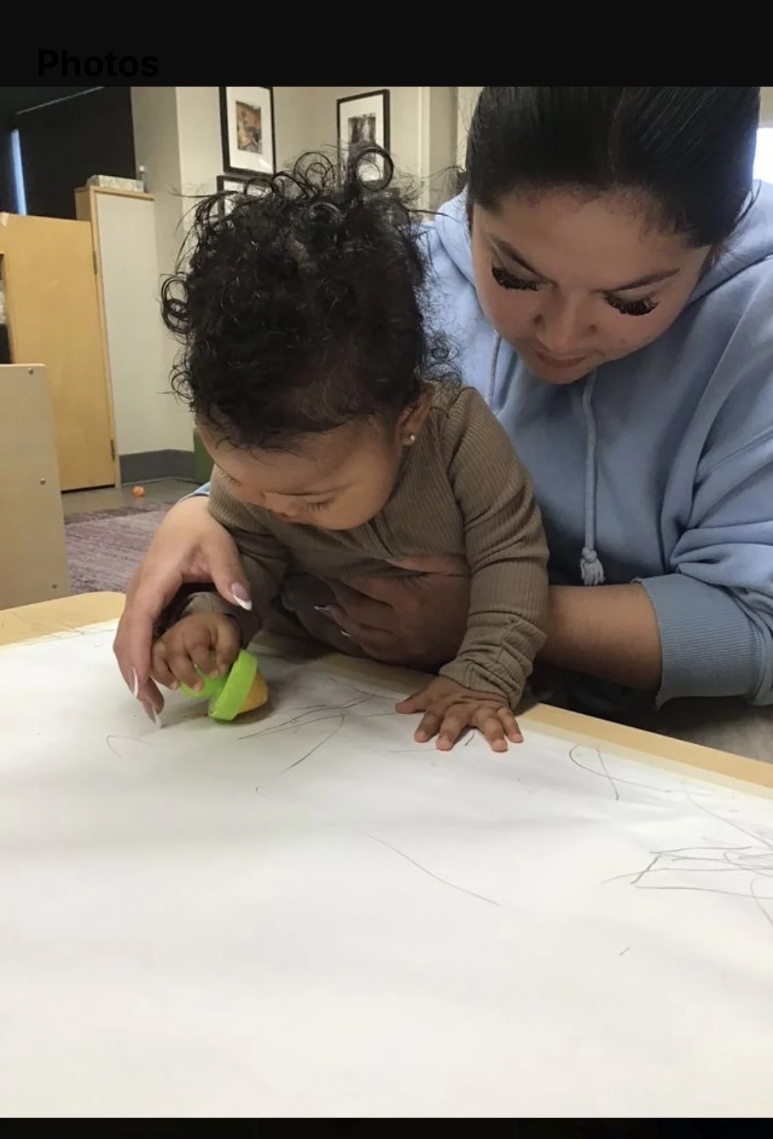 Young child colours on paper while an educator holds them steady.